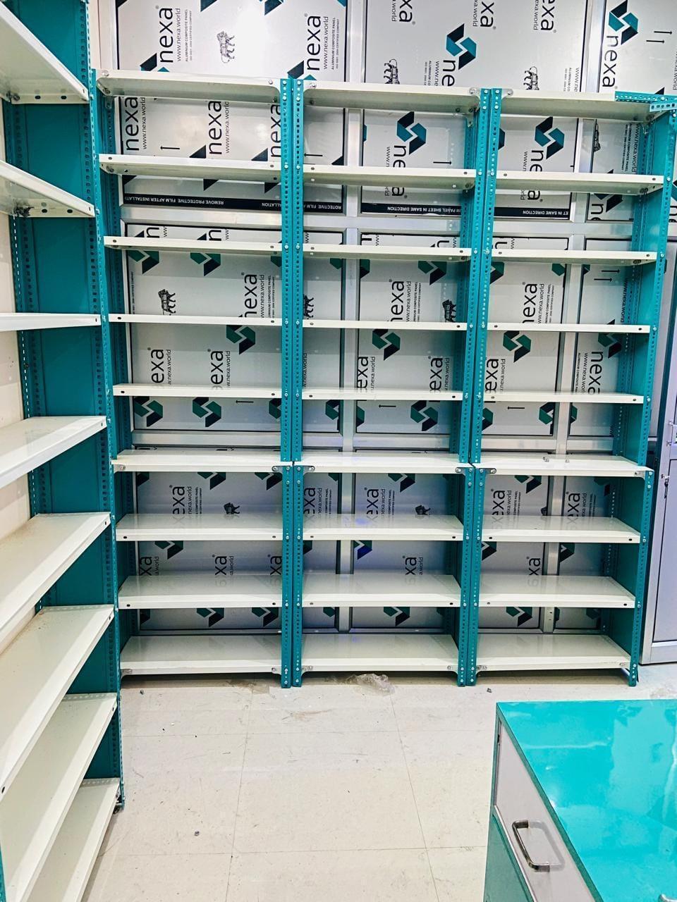 Three bays of white shelves on teal uprights in a medical store, set close together